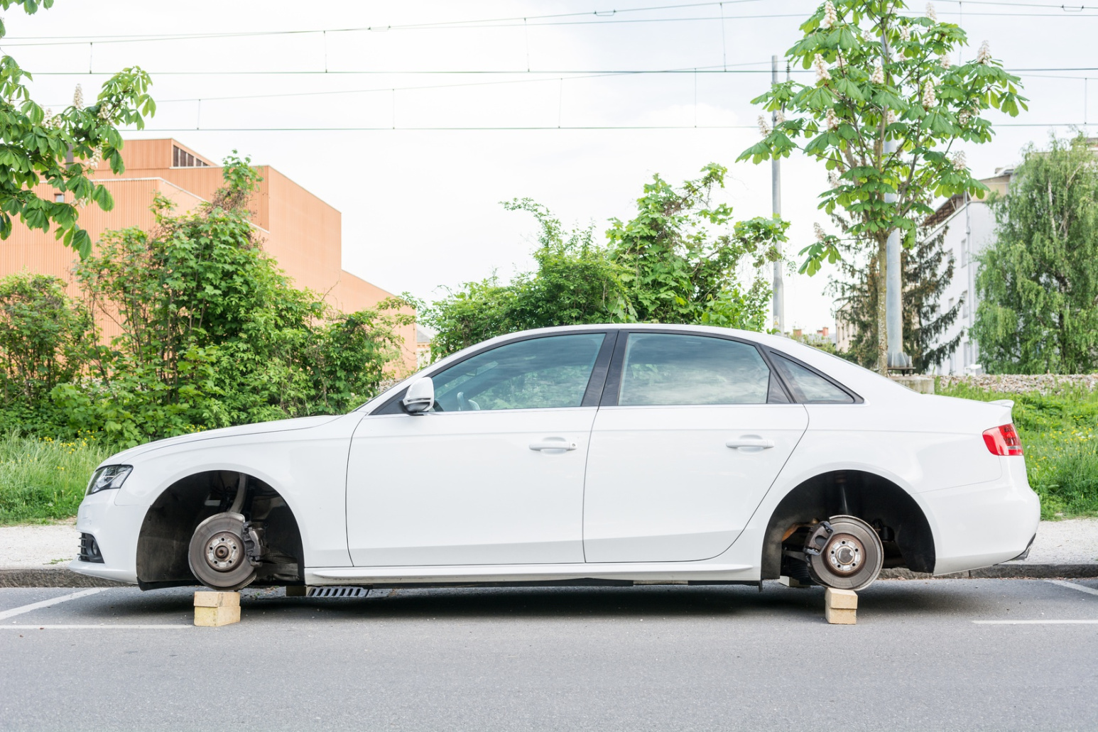 Weißes Auto mit gestohlenen Rädern, das auf Holzblöcke aufgebockt wurde; Kurtz Detektei Hamburg, Detektiv in Hamburg, Wirtschaftsdetektei in Hamburg, Detektivagentur in Hamburg